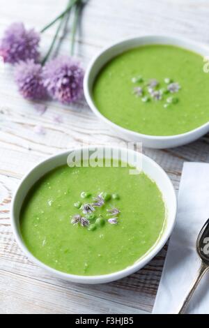 Ancora in vita di zuppa di piselli servito con erba cipollina fresca e fiori di erba cipollina Foto Stock