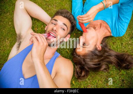 Donna matura e giovane, giacente su erba, mangiando ghiaccioli, vista aerea Foto Stock