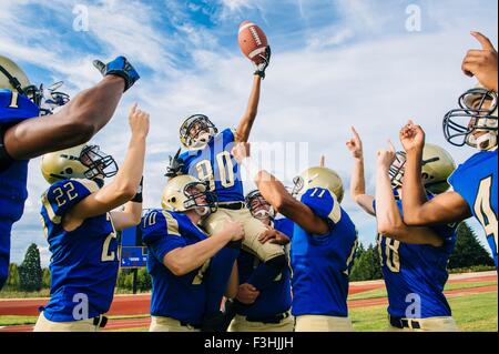 Un adolescente e giovane maschio american football team celebrando insieme sul campo di calcio Foto Stock