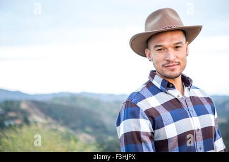 Ritratto di giovane uomo che indossa il cappello da cowboy sulla collina rurale Foto Stock