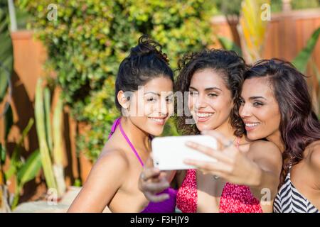 Tre sorelle adulte indossando un bikini tops in posa per smartphone selfie in giardino Foto Stock