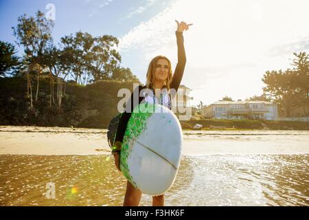 Giovane donna in piedi in mare, affacciato sul mare, tenendo le tavole da surf, gesti con le mani Foto Stock