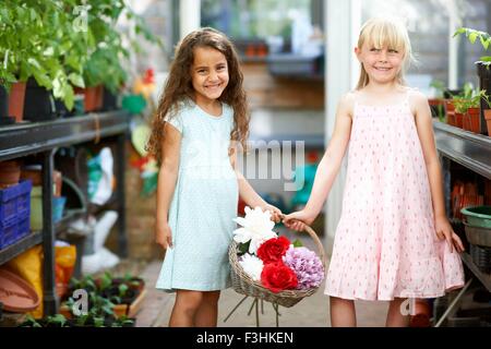 Ritratto di due ragazze cestello di contenimento di fiori freschi in serra Foto Stock