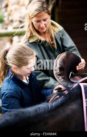 Donna matura e figlia saddling cavallo Foto Stock