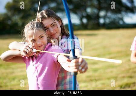 Ragazza di tiro con l'arco di apprendimento dalla sorella adolescente Foto Stock