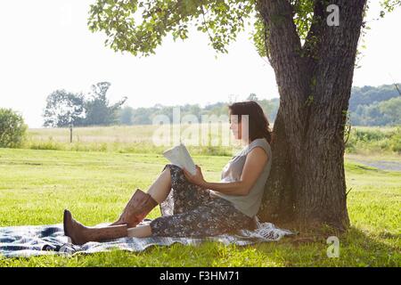 Donna libro lettura mentre appoggiata ad albero Foto Stock