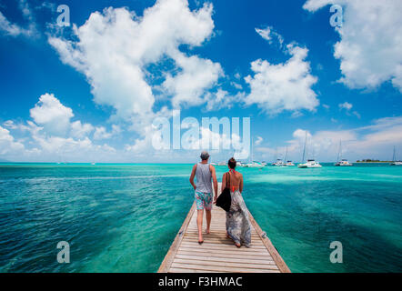 ANEGADA ISLAND, Isole Vergini Britanniche, Isole dei Caraibi. Un giovane cammina per un lungo molo circondato da teal mare e cielo blu. Foto Stock