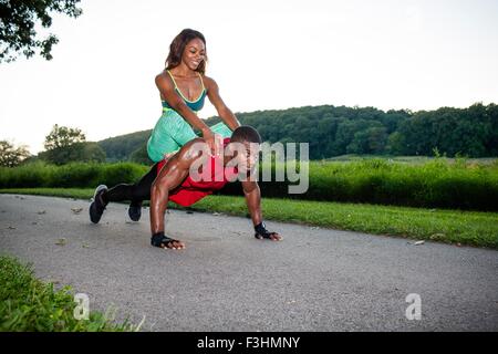 Giovane uomo che fa pushups sulla strada rurale offrendo nel contempo ragazza un piggyback Foto Stock