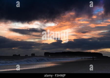 Un tramonto tempestoso guardando a Dyrhólaey, Islanda con impressionante di onde che si infrangono sulla spiaggia sassosa con un drammatico sky Foto Stock