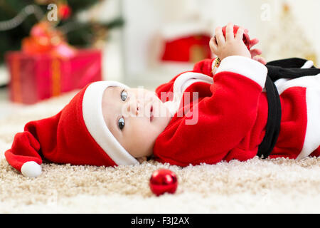 Baby boy usurata Santa che giace nei pressi di albero di Natale Foto Stock