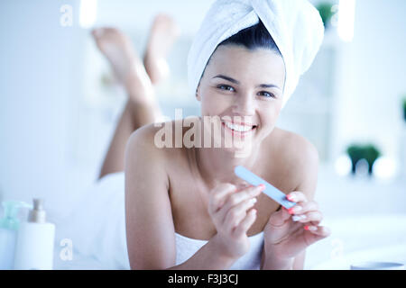 Piuttosto giovane donna prendendo cura di lei le unghie dopo il bagno Foto Stock