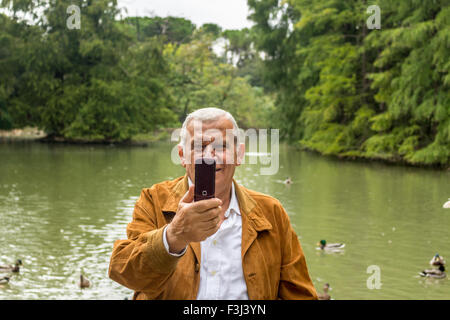 Senior con Giacca scamosciata e camicia bianca in un verde parco prende selfie Foto Stock