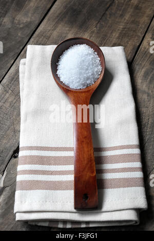 Il sale di mare in un cucchiaio di legno su tavola in legno rustico Foto Stock