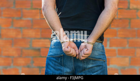 Arresto, close-up shot mani dell'uomo con le manette di fronte di terracotta Mattoni parete con copy-spazio Foto Stock