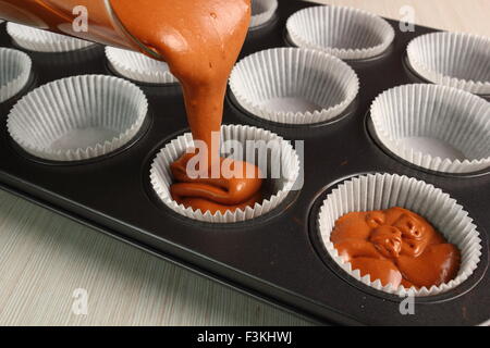 Versando cake mix in padella. Fare muffin al cioccolato. Foto Stock