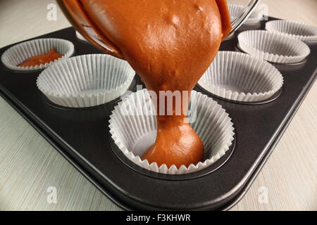 Versando cake mix in padella. Fare muffin al cioccolato. Foto Stock