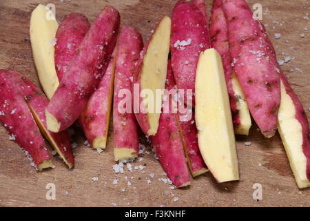 Dolce giapponese di patate tagliate lengthwish su un tagliere di legno e poi spruzzata con seasalt; pronto per essere fritto. Foto Stock