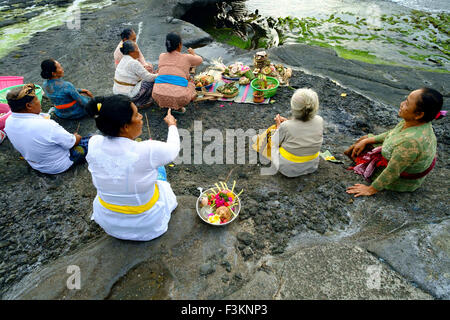 Balinese devoti Indù pregare al tramonto sulle spiagge rocciose attorno al dal Tempio Tanah Lot. Foto Stock