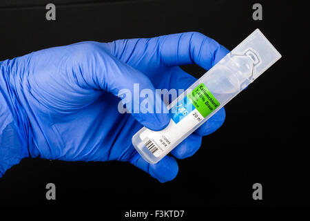 Una mano in una blu guanto medicale è in possesso di una bottiglia di plastica contenente cloruro calium per uso medico, visualizzato su una tavola nera Foto Stock