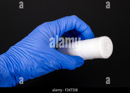 Una mano in una blu guanto medicale è in possesso di un bianco Benda di garza per uso medico, visualizzato su una tavola nera Foto Stock