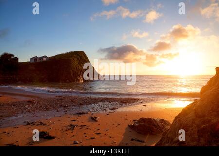 Cabine sulla spiaggia, sulla scogliera cime con il sole che tramonta sulla speranza Cove, Devon, Inghilterra Foto Stock