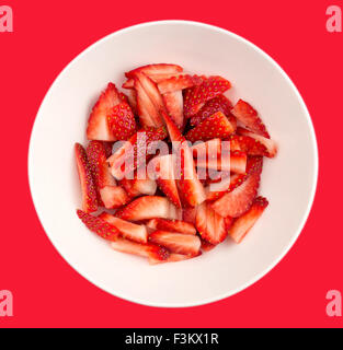 Fresche fragole a fette in un bianco rotondo ciotola contro uno sfondo di colore rosso. Foto Stock