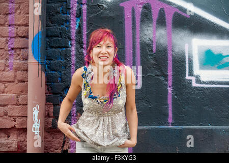 Giovane bella ragazza in harajuku stile con capelli colorati e freaky outfit davanti al muro con la street art pittura Foto Stock