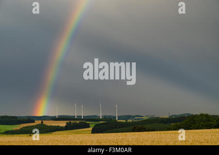 Impianti di energia eolica dietro un grainfield con cielo nuvoloso scuro e rainbow Foto Stock