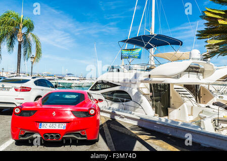 Ferrari e altri sport auto parcheggiate accanto ai lussuosi yacht ormeggiati a Puerto Banus, un marina vicino a Marbella, Andalusia, Spagna Foto Stock