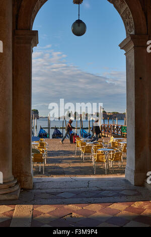 I turisti wheeling valigie lungo waterfront presso sunrise visto dal corridoio colonnato in Piazzetta San Marco Venezia Italia Foto Stock