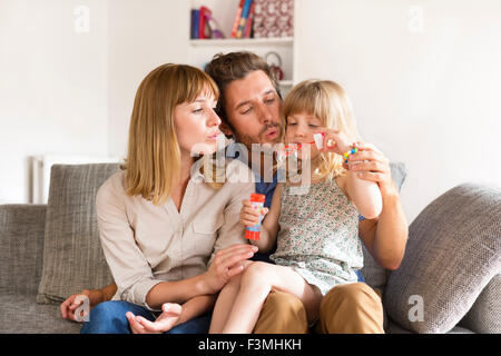 Allegro i genitori e la figlia a soffiare bolle in bianco casa moderna Foto Stock