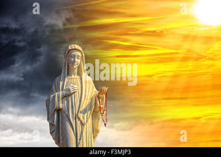 Una statua della Vergine Maria contro un cielo drammatico. Foto Stock