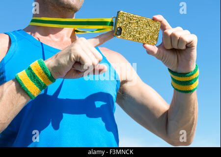 Atleta brasiliano con il verde ed il giallo polsini con medaglia d oro telefono mobile contro il cielo blu Foto Stock