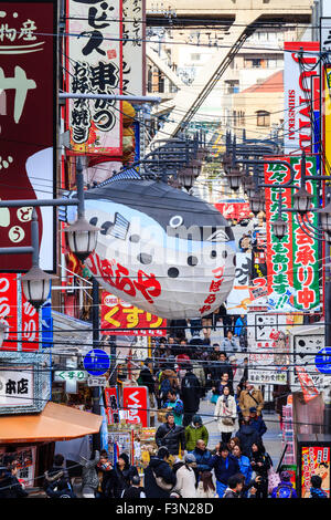 Shinsakei, Osaka. Famoso il pesce palla, fugu, segno appeso con sfondo occupato di segni, bar, negozi lungo la strada principale nella zona di intrattenimento. Foto Stock