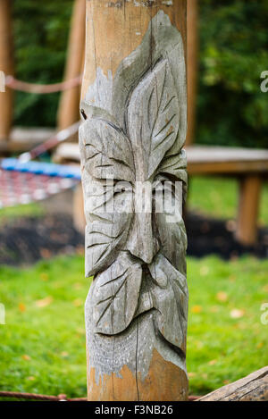 Frondose il volto dell'uomo intagliato in un palo di legno in un parco giochi per bambini. Wolverton Mill, Milton Keynes, Regno Unito. Foto Stock