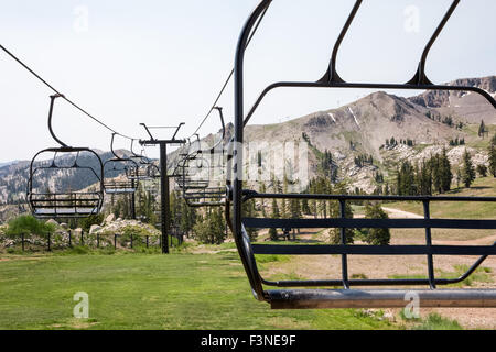 Svuotare ski lift sedie inattivi durante l'estate. Il fuoco selettivo sulla sedia in primo piano. Robusto collina di sci in background. Foto Stock