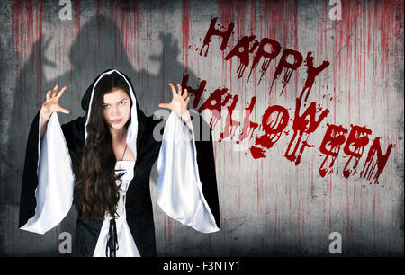 Happy halloween spruzzata su una sanguinosa muro accanto alla ragazza vestita come una strega Foto Stock