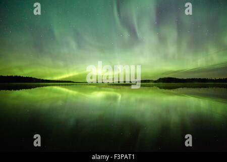 Luci del nord (Aurora Boreale) al di sopra di un lago con acqua ancora e riflessioni a notte. Stelle del cielo notturno dietro il Pola Foto Stock