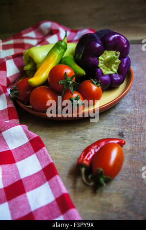 Mature verdura fresca di pomodori ciliegini, Campana e peperoncino piccante, cipolla, sfondo rustico Foto Stock