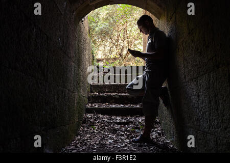 Giovane uomo lavora su uno smartphone in pietra scura tunnel Foto Stock