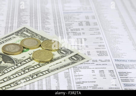 Un dollaro nota, British una libbra e una delle monete in euro su una carta di notizie del mercato azionario pagina finanziaria mostra titoli e azioni Foto Stock