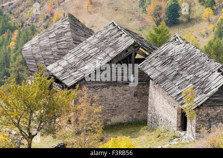 Vecchio danneggiato i tetti in legno in larice di tavole che copre tre chalets abbandonati nelle Alpi Italiane Foto Stock