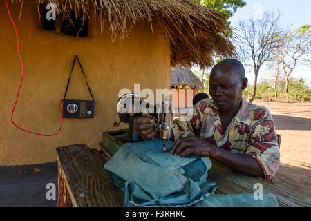 L'uomo con la macchina da cucire davanti a una capanna, Zambia, Africa Foto Stock