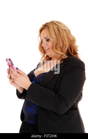 Una bionda plus dimensione donna di affari in una giacca nera che si occupano sul suo telefono cellulare, in piedi nel profilo isolato per sfondo bianco. Foto Stock