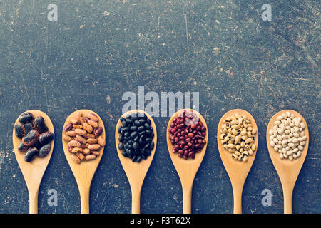 Diversi legumi crudi in cucchiai di legno Foto Stock