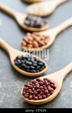 Diversi legumi crudi in cucchiai di legno Foto Stock