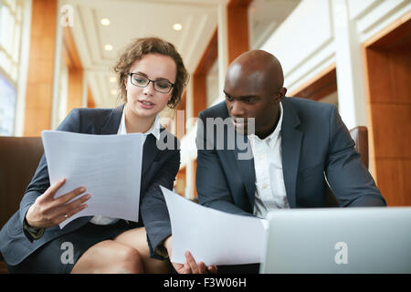 Ritratto di giovane uomo di affari e donna seduta al cafe e discutere di contratto. Diversi imprenditori incontro nella hall hotel Foto Stock