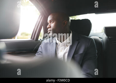 Giovane africano uomo d'affari in viaggio per lavoro in auto di lusso sul sedile posteriore di guardare fuori dalla finestra. Foto Stock