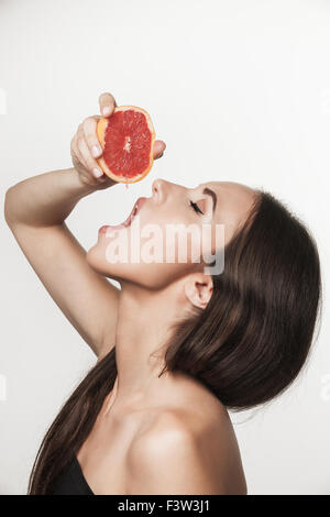 Giovane e bella bruna donna che mantiene fresco affettato pompelmo e spremendo il succo fresco fuori di esso. Mangiare sano stile di vita e Foto Stock
