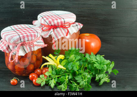 Vasetti di ketchup fatti in casa e pomodoro ciliegino accanto a freschi pomodori ciliegia su sfondo scuro Foto Stock